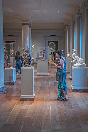 A visitor in a flowing dress stands thoughtfully among the sculptures on display at the National Gallery's sculpture hall.