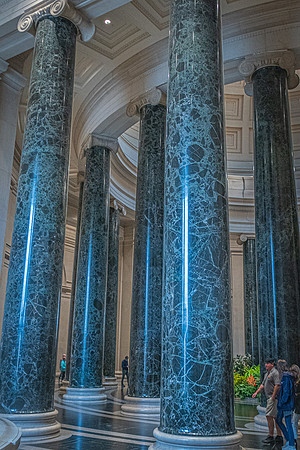 Marble columns with intricate veining stand tall in the National Gallery, with visitors walking by, showcasing the grand architecture.