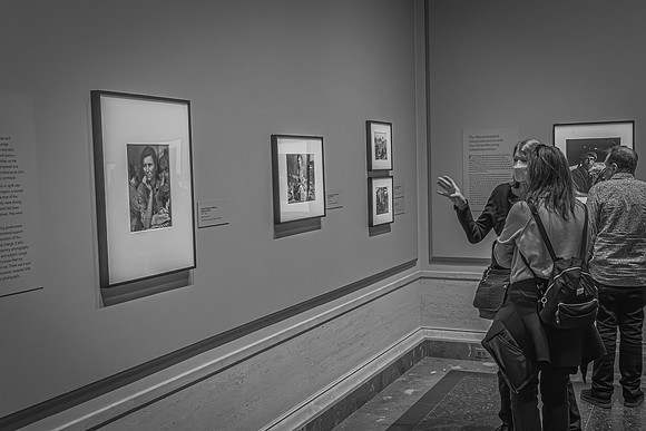 Visitors at the Dorothea Lange exhibition discussing her famous "Migrant Mother" photograph, alongside other historical black-and-white photographs on display.