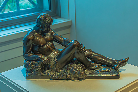 A reflective bronze sculpture of a seated figure, highlighted by natural light, on display at the National Gallery.